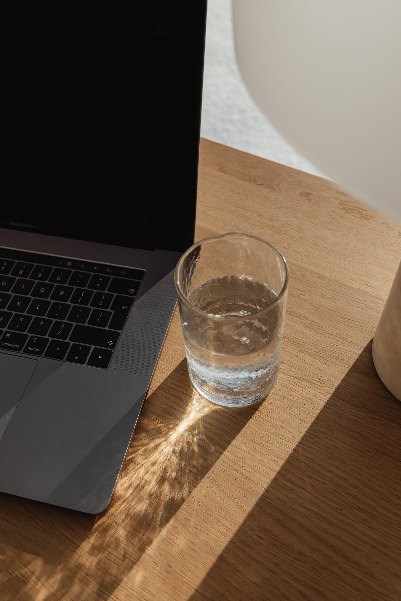 Ordinateur portable et verre d'eau posés sur un bureau en bois clair